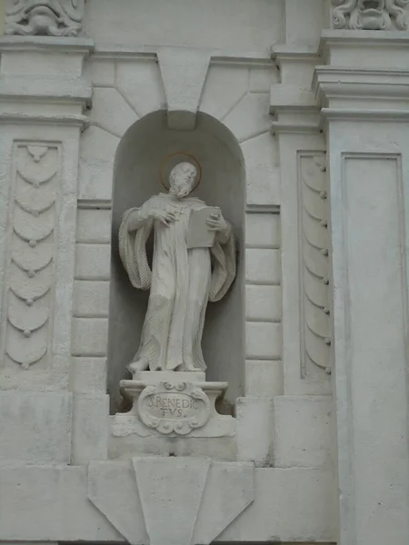 A statue of the saint in white marble with a golden halo standing in an arch on the wall of the building — Stock Image Statue Saint White Marble Golden Halo Standing Arch Wall Building Royalty Free Stock Images