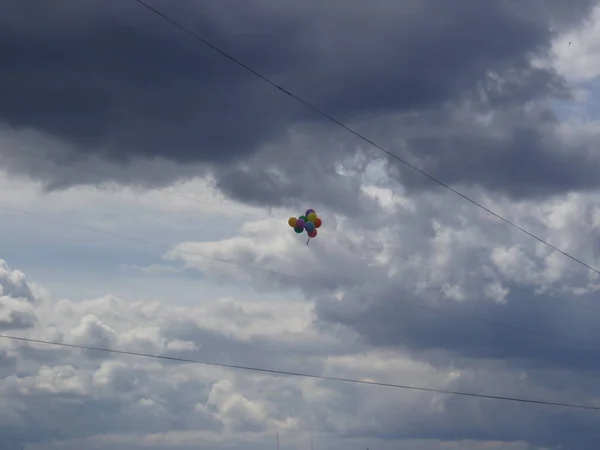 Bir kucak dolusu renkli balon, kümülüs gri bulutlarının arka planına kablolar takılmış.