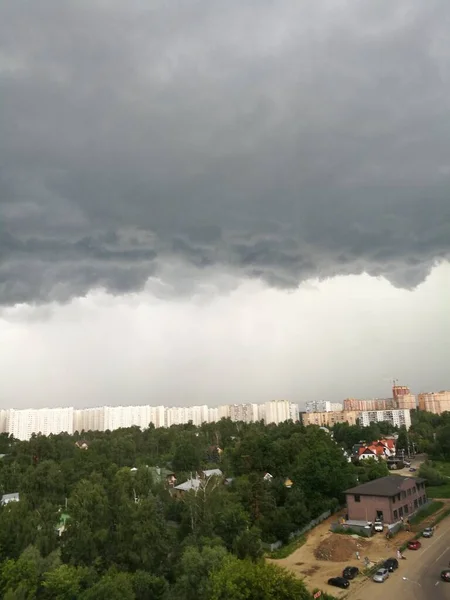 Yeşil ağaçlar ve alçak binalar üzerinde asılı koyu gri fırtına bulutları