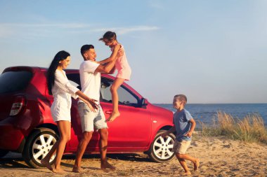 Mutlu bir aile kumsalda arabanın yanında eğleniyor. Yaz gezisi