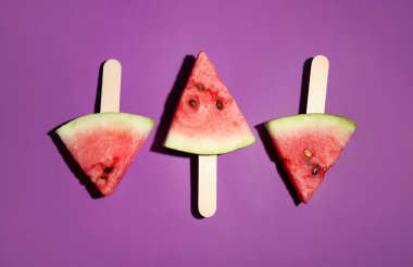 Mor zemin üzerinde tahta çubuklar olan karpuz dilimleri, düz uzanmış.