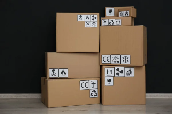 黒い壁の近くの床の上に異なる包装シンボルを持つ段ボール箱 小包の配達 — ストック写真