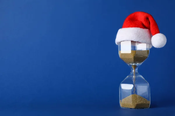 Hourglass Και Σάντα Καπέλο Μπλε Φόντο Χώρος Για Κείμενο Χριστουγεννιάτικη — Φωτογραφία Αρχείου