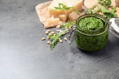 Lezzetli roka pesto kavanozu ve gri masadaki malzemeler. Metin için boşluk