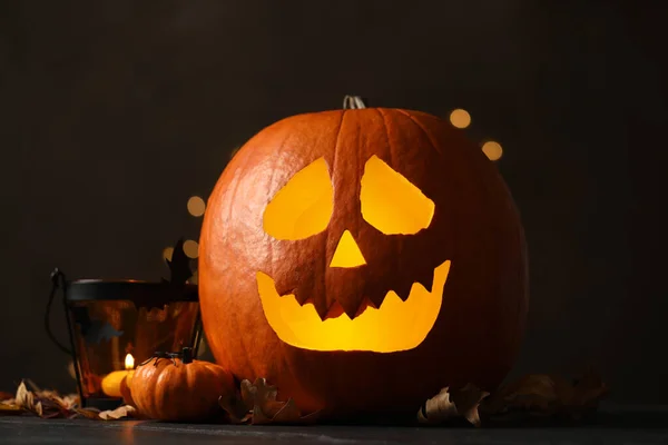 Pumpkin jack o\'lantern and Halloween decor on table against dark background