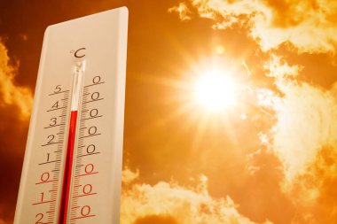 Hava durumu termometresi arka planda bulutlu ve güneşli gökyüzünü gösteriyor