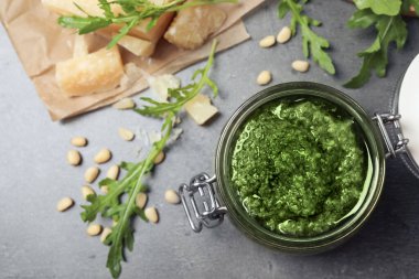 Lezzetli roka pesto kavanozu ve gri masadaki malzemeler düz.