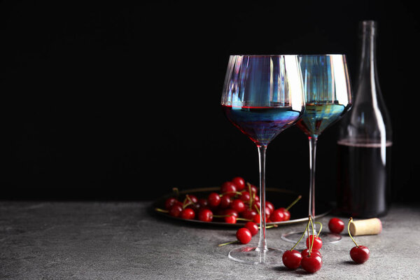 Delicious cherry wine and ripe juicy berries on grey table against black background. Space for text