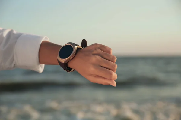 Young woman checking smart watch on beach at sunset, closeup