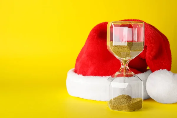 Hourglass Και Σάντα Καπέλο Κίτρινο Φόντο Χώρος Για Κείμενο Χριστουγεννιάτικη — Φωτογραφία Αρχείου