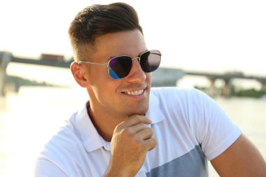 Nehir kenarında şık güneş gözlüğü takan yakışıklı bir adam.