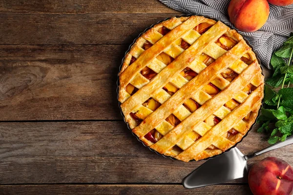 Delicious peach pie and fresh fruits on wooden table, flat lay. Space for text