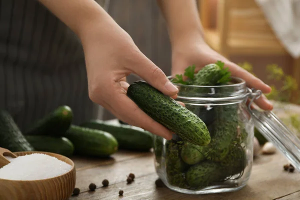 Woman putting cucumber into glass jar at wooden kitchen table, closeup. Pickling vegetables — Stock Image Woman Putting Cucumber Glass Jar Wooden Kitchen Table Closeup Pickling Royalty Free Stock Images