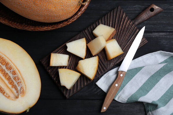 Pieces of delicious honey melon on black wooden table, flat lay