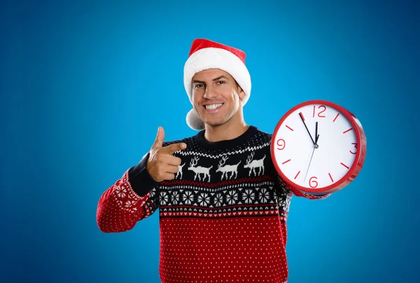 サンタの帽子の男は青い背景に時計をつけている 新年のカウントダウン — ストック写真