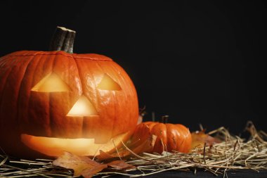 Balkabağı Jack O 'Lantern, saman ve sonbahar yaprakları karanlıkta masada, yazı için yer var. Cadılar Bayramı Dekorasyonu