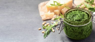Bir kavanoz roka roka pesto ve gri masada malzemeler, yazı için yer. Pankart tasarımı 