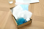 Lepenková krabice s antiseptiky a respiračními maskami na dřevěném stole. Ochranné prvky při pandemii COVID-19