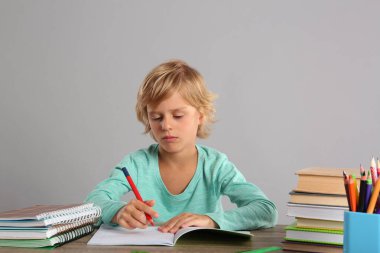 Küçük çocuk gri arka planla ilgili ödev yapıyor.