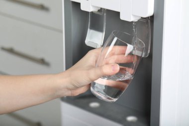 Bardağı su soğutucusuyla dolduran kadın, yakın plan. Tazeleyici içecek.