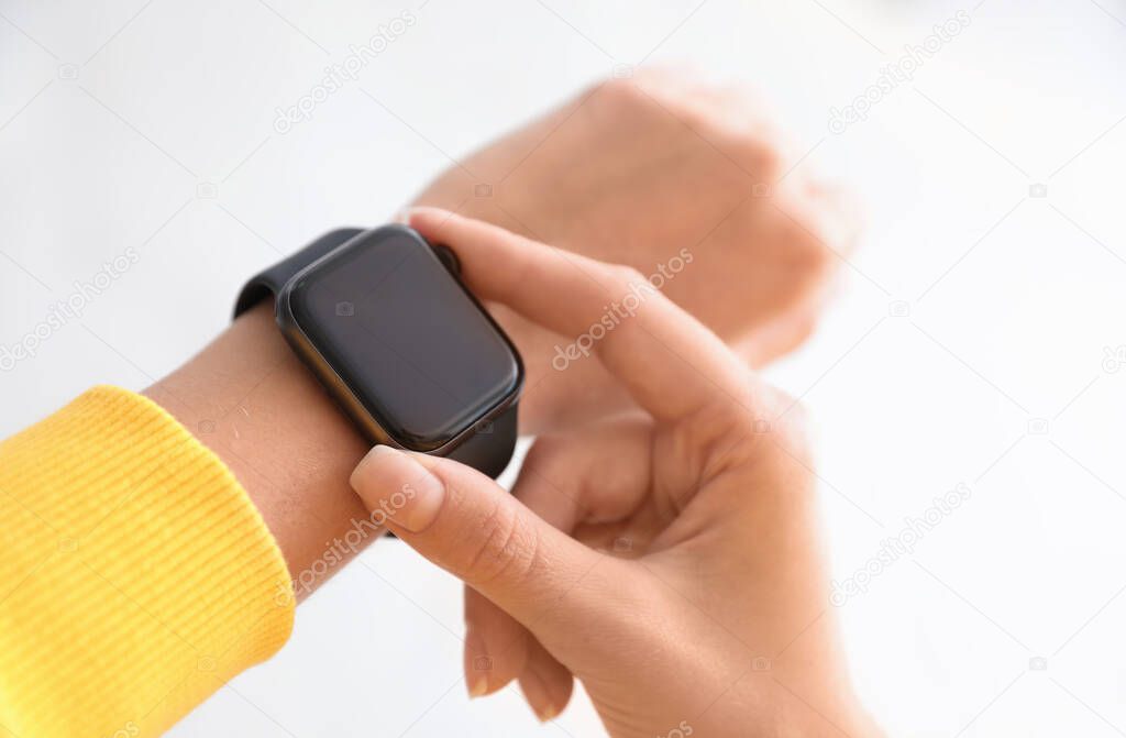 Woman checking stylish smart watch on light background, closeup