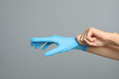 Gri arka planda tıbbi eldiven giyen doktor, yakın plan.