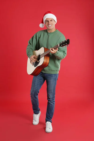 Чоловік Капелюсі Санта Грає Акустичній Гітарі Червоному Тлі Різдвяна Музика — стокове фото