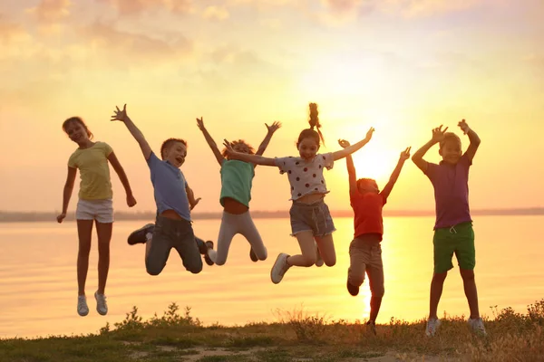 Szczęśliwe Małe Dzieci Skaczące Pobliżu Rzeki Zachodzie Słońca — Zdjęcie stockowe