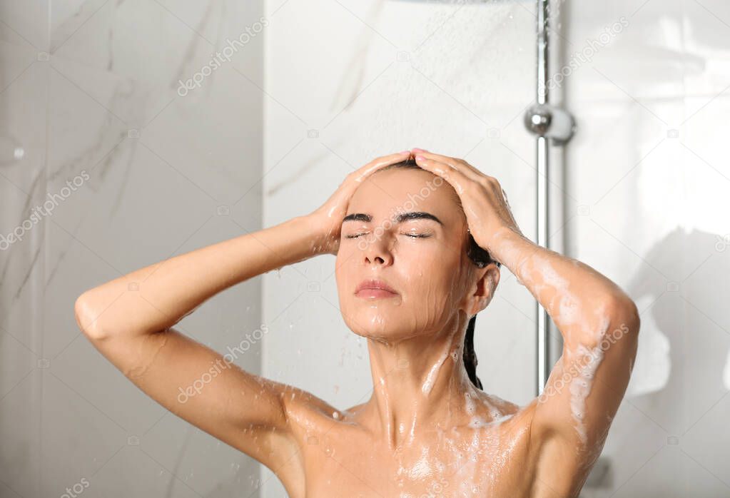 Beautiful young woman washing hair in shower at home