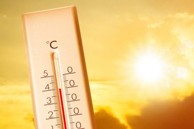 Hava durumu termometresi arka planda bulutlu ve güneşli gökyüzünü gösteriyor