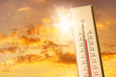 Hava durumu termometresi arka planda bulutlu ve güneşli gökyüzünü gösteriyor