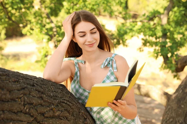 Young woman reading book on tree in park