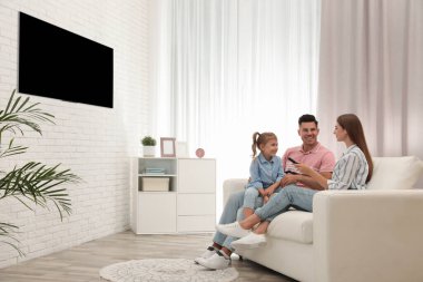 Mutlu bir aile evdeki kanepede televizyon izliyor.