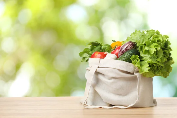 Fresh vegetables in cloth bag on wooden table against blurred background. Space for text