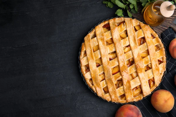 Delicious peach pie and fresh fruits on black table, flat lay. Space for text