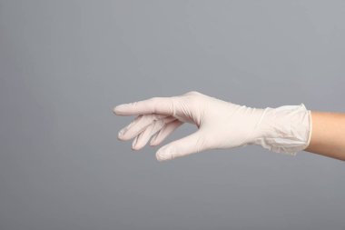 Gri arka planda tıbbi eldiven giyen doktor, yakın plan.