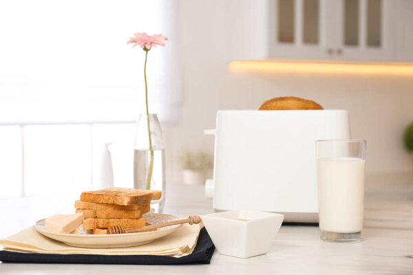 Modern toaster and tasty breakfast on white marble table in kitchen