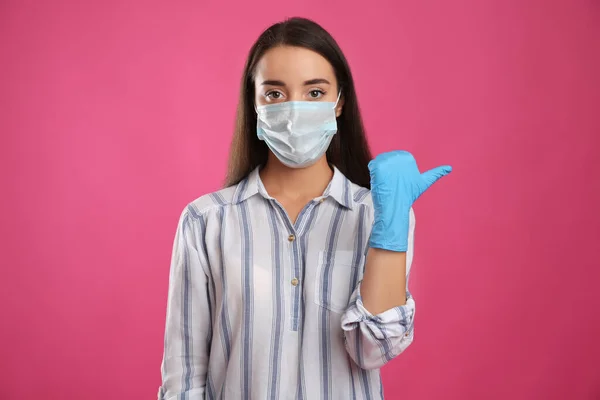 Kvinna Skyddande Ansiktsmask Och Medicinska Handskar Pekar Något Rosa Bakgrund — Stockfoto