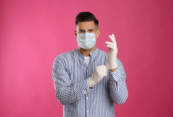Man Skyddande Ansiktsmask Sätta Medicinska Handskar Mot Rosa Bakgrund — Stockfoto