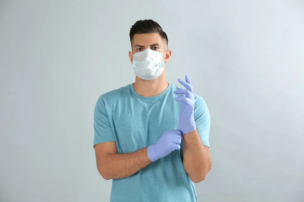 Man Skyddande Ansiktsmask Sätta Medicinska Handskar Mot Grå Bakgrund — Stockfoto