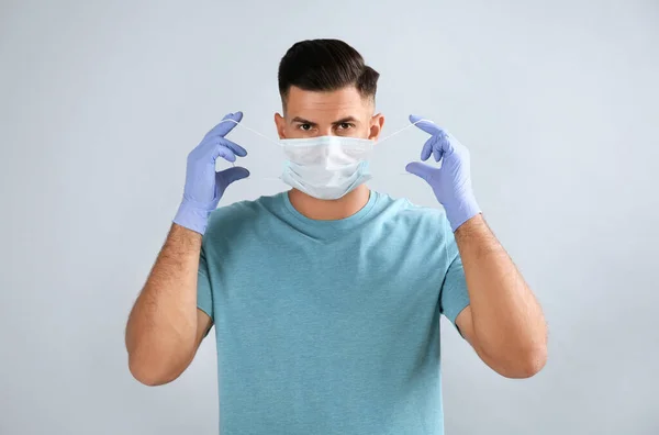 Man Medicinska Handskar Sätta Skyddande Ansiktsmask Mot Grå Bakgrund — Stockfoto