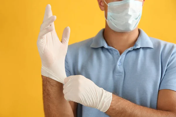 Man Skyddande Ansiktsmask Sätta Medicinska Handskar Mot Gul Bakgrund Närbild — Stockfoto