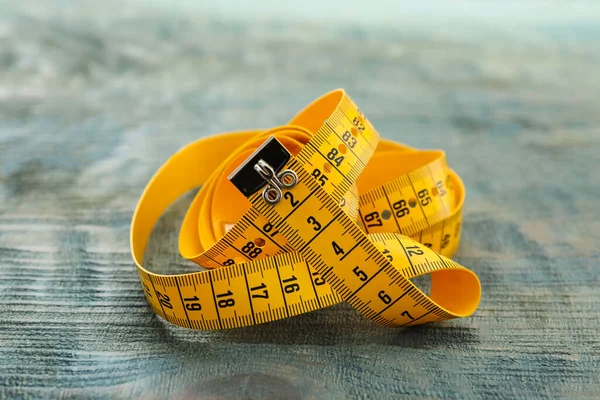 Yellow measuring tape on light blue wooden table, closeup