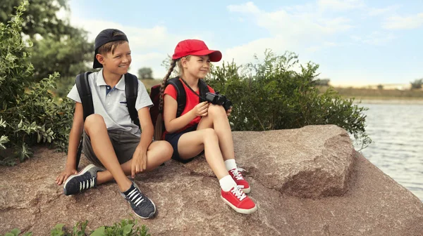 Lindos Niños Pequeños Con Mochilas Sentadas Roca Cerca Del Río —  Fotos de Stock