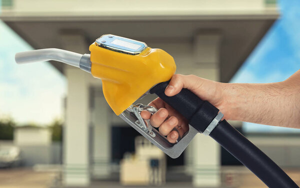 Man holding fuel nozzle near gas station, closeup