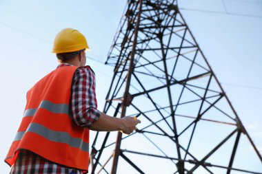 Yüksek voltaj kulesinin yanında telsizi olan elektrik mühendisi, düşük açılı görüş.