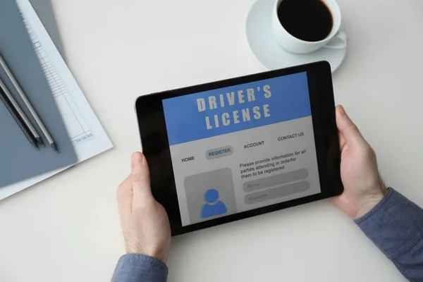Man holding tablet with driver's license application form at white table, above view