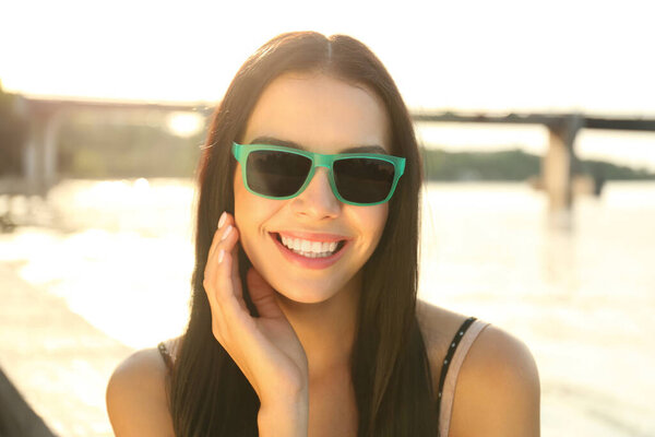 Красивая молодая женщина в стильных солнечных очках возле реки