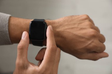 Gri arkaplanda şık akıllı saati kontrol eden adam, yakın plan