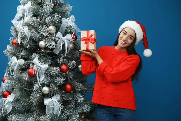 Счастливая Молодая Женщина Шляпе Санта Клауса Подарком Возле Елки Голубом — стоковое фото